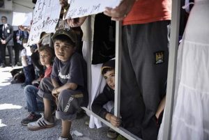 In this photo released by Greek Prime Minister's office on Saturday, April 16, 2016, refugees and migrants look on during a visit by Ecumenical Patriarch Bartholomew I, Pope Francis, and Greek Orthodox Archbishop Ieronymos at the Moria refugee camp on the island of Lesbos, Greece. Pope Francis implored Europe on Saturday to respond to the migrant crisis on its shores "in a way that is worthy of our common humanity," during an emotional and provocative trip to Greece.  (Andrea Bonetti/Greek Prime Minister's Office via AP)