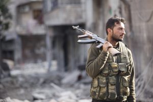 A FREE SYRIAN ARMY FIGHTER HOLDS HIS RIFLE AS HE STANDS ON A DAMAGED STREET  IN ALEPPO'S KARM AL-JABAL DISTRICT